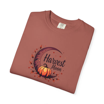 A folded terracotta-colored t-shirt with a 'Harvest Moon' graphic featuring a crescent moon, autumn leaves, and a pumpkin, displayed on a clean white background.