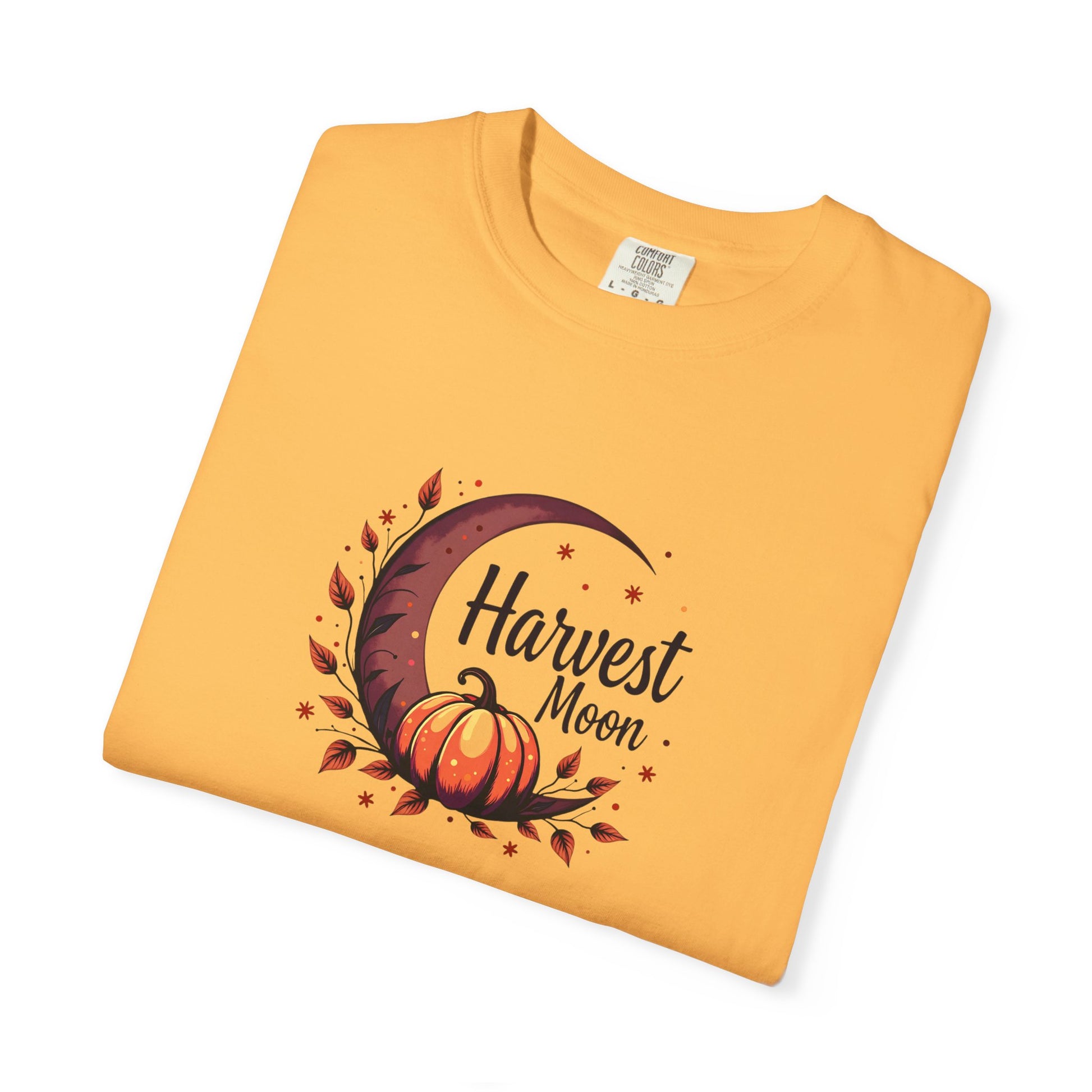 A folded citrus orange t-shirt with a 'Harvest Moon' graphic featuring a crescent moon, autumn leaves, a pumpkin, and stars, displayed on a clean white background.