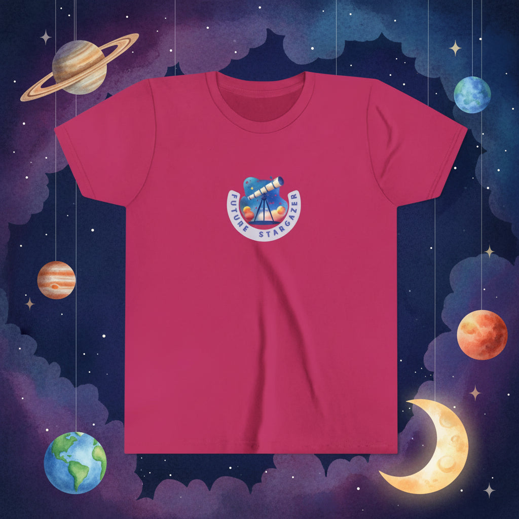 A berry pink short-sleeve crewneck t-shirt featuring a colorful 'Future Stargazer' telescope graphic printed on the center chest, displayed against a background with model planets and moon hanging from the ceiling. Malika Bourne Legacy design