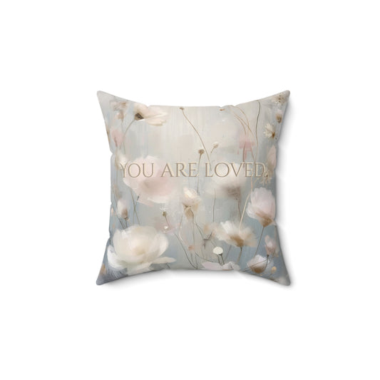 Decorative pillow with floral design and 'YOU ARE LOVED' text on a white background