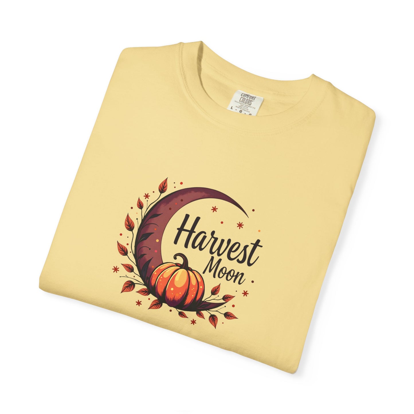 A folded butter/ pale yellow t-shirt with a 'Harvest Moon' graphic featuring a crescent moon, autumn leaves, a pumpkin, and stars, displayed on a clean white background.