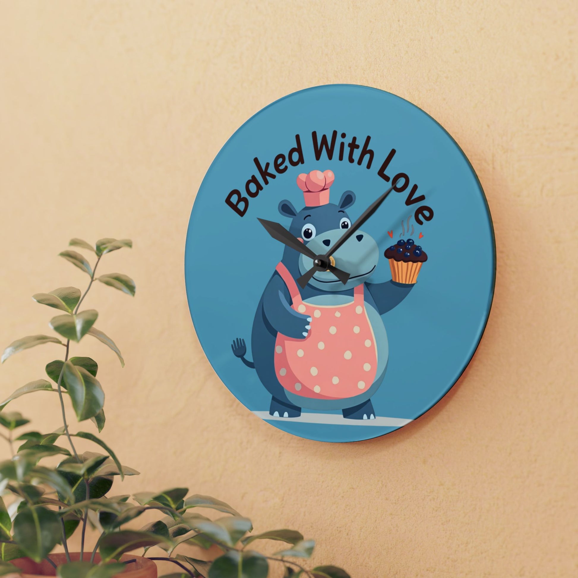 Wall clock with cartoon hippo holding a cupcake and text 'Baked With Love' on a beige wall.