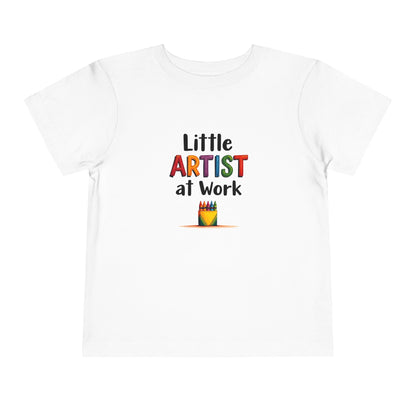 A white short-sleeve toddlers' t-shirt with a colorful graphic on the chest that reads 'Little ARTIST at Work' above a small crayon box illustration, shown on a plain white background.
