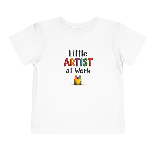 A white short-sleeve toddlers' t-shirt with a colorful graphic on the chest that reads 'Little ARTIST at Work' above a small crayon box illustration, shown on a plain white background.