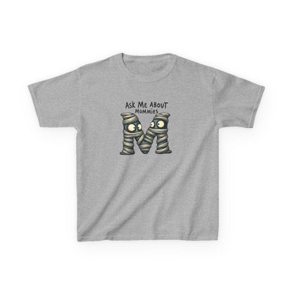 Kids history-themed shirt with “Ask Me About Mummies” design featuring cartoon mummy lettering on a Gildan 5000B Heavy Cotton Tee. Sport Grey