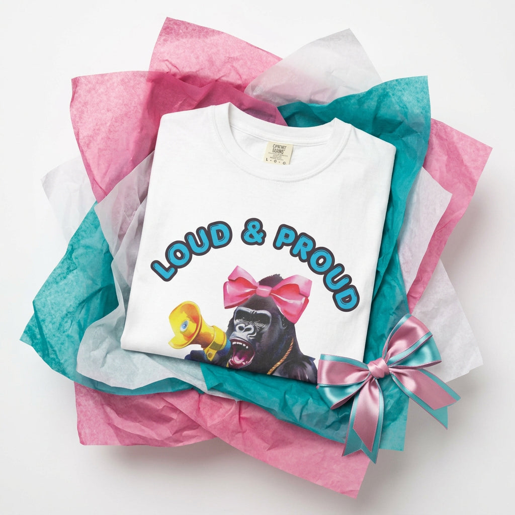 Folded white tee. “Girl‑Girl™ cheerleader gorilla with pink bow and megaphone on a white unisex tee with the phrase ‘Loud & Proud.’”