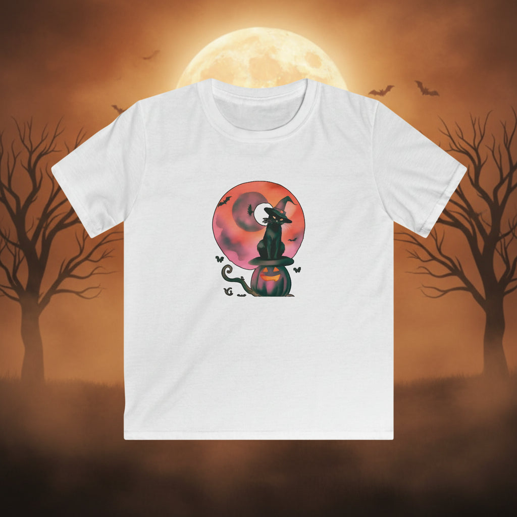 A white short-sleeve crewneck t-shirt featuring a Halloween graphic of a black witch cat sitting on a jack-o'-lantern pumpkin in front of a pink and orange full moon.