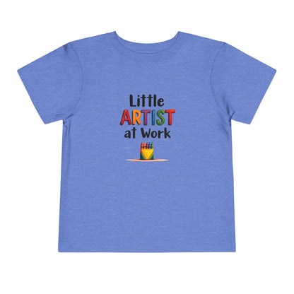 A heather blue short-sleeve toddlers' t-shirt with a colorful graphic on the chest that reads 'Little ARTIST at Work' above a small box of crayons illustration, shown on a plain white background.