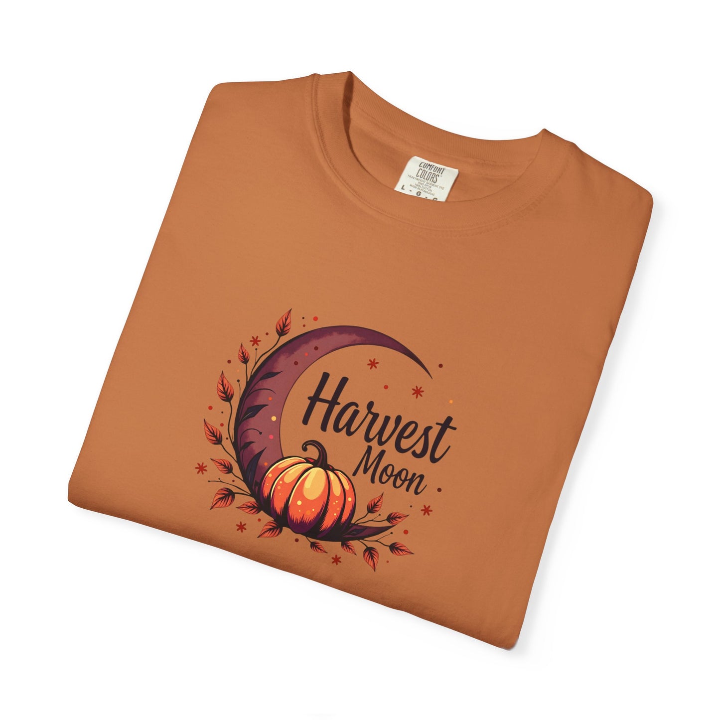 A folded terracotta/ orange crewneck t-shirt with a 'Harvest Moon' graphic featuring a crescent moon, autumn leaves, and a pumpkin on a white background.