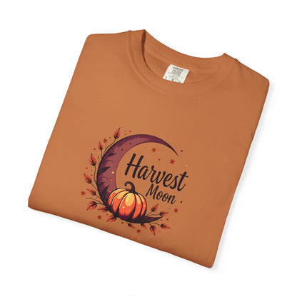 A folded terracotta/ orange crewneck t-shirt with a 'Harvest Moon' graphic featuring a crescent moon, autumn leaves, and a pumpkin on a white background.