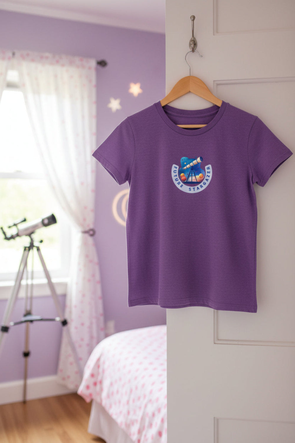 A purple short-sleeve t-shirt with a circular graphic on the center chest featuring a telescope design with the text 'Future Stargazer." Malika Bourne Legacy design