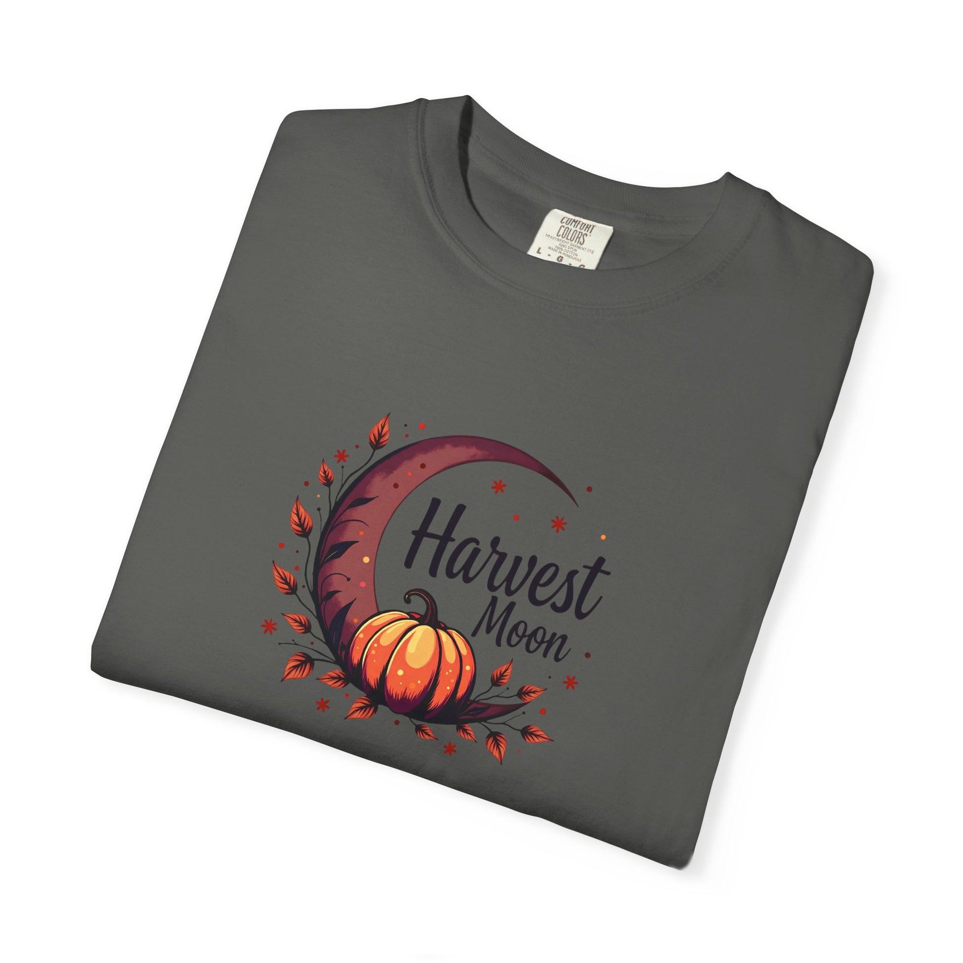 A folded dark sage green t-shirt with a 'Harvest Moon' graphic featuring a crescent moon, autumn leaves, a pumpkin, and stars, displayed on a clean white background.