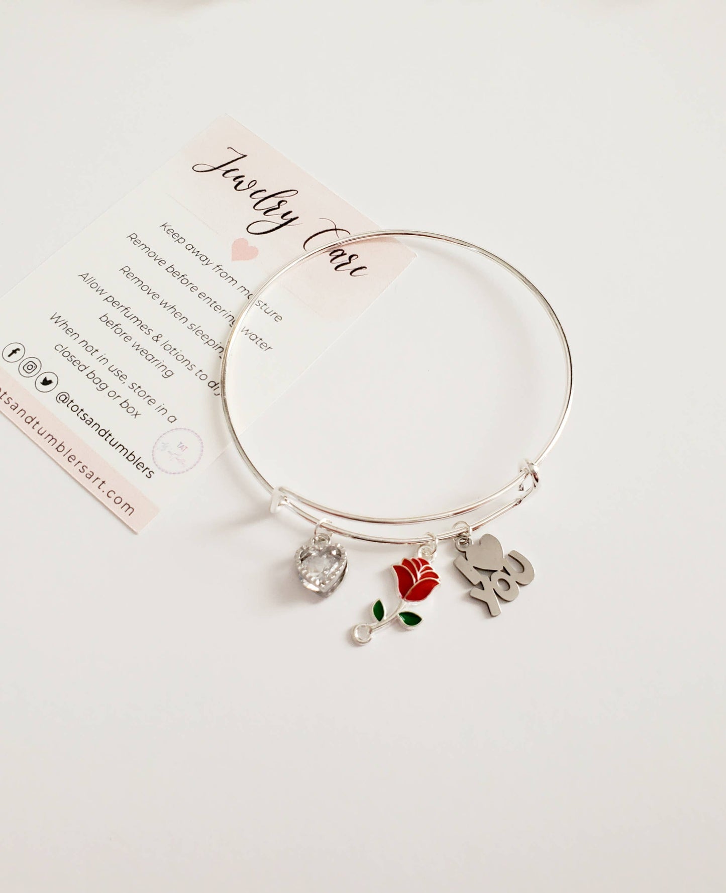 Silver bracelet with charms on a white background with jewelry care instructions.
