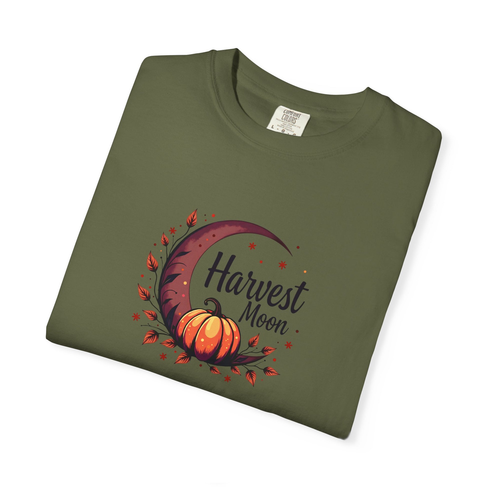 An olive green folded t-shirt with a 'Harvest Moon' graphic featuring an orange pumpkin, crescent moon, and autumn leaves on a white background.