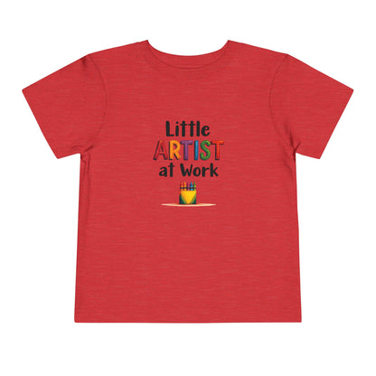 A red heather short-sleeve toddler's t-shirt with a colorful graphic on the chest that reads 'Little ARTIST at Work' above a small box of crayons shown on a plain white background.