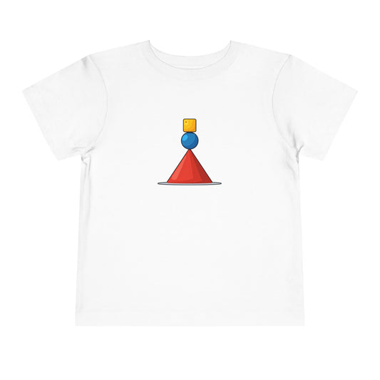 A white short-sleeve crewneck t-shirt featuring a central graphic of a red cone balanced on a blue sphere, which is topped by a small yellow square, all resting on a thin gray line.