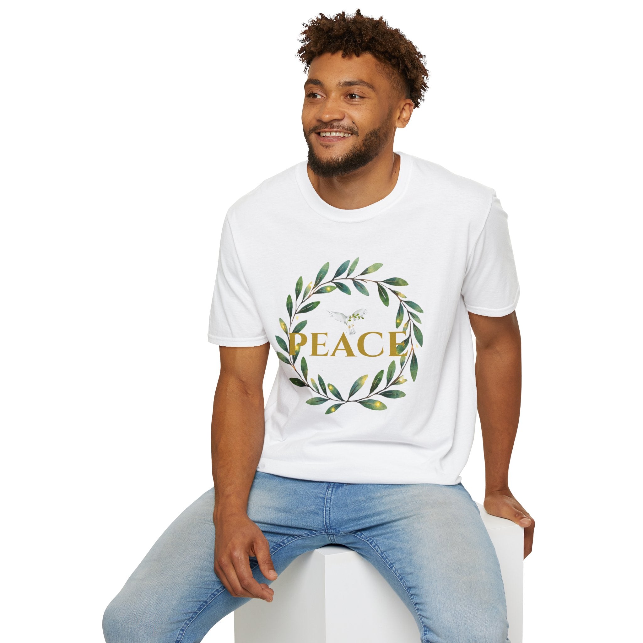 Man sitting wearing Classic Gildan Softstyle t‑shirt with a watercolor olive‑leaf wreath and gold PEACE lettering, shown in white.