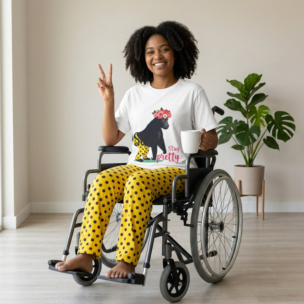 AI model wears the shirt. “Girl‑Girl™ gorilla wearing a flower crown and patterned shorts on a white unisex tee with the phrase ‘Stay Pretty.’” AI model sits in a wheelchair and wears AI-generated pants that match what the tee gorilla character is wearing: yellow pants with block dots.