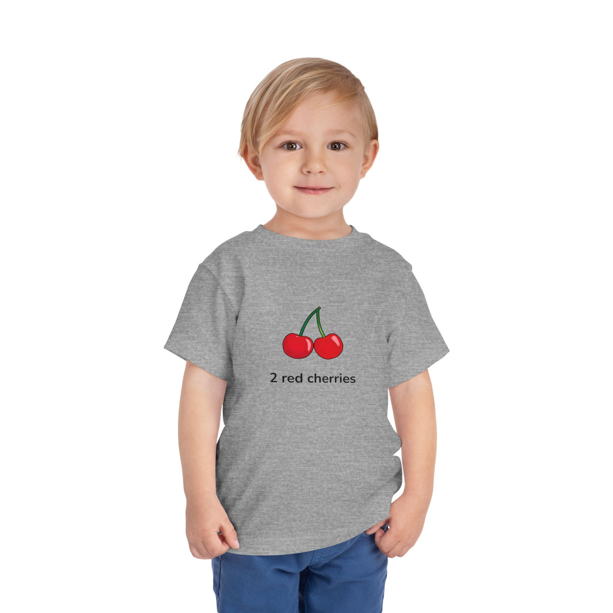 A young child wearing a heather gray graphic T-shirt with the text 'SMALL BUT MIGHTY.' in black and red, paired with blue pants, standing against a plain white background.