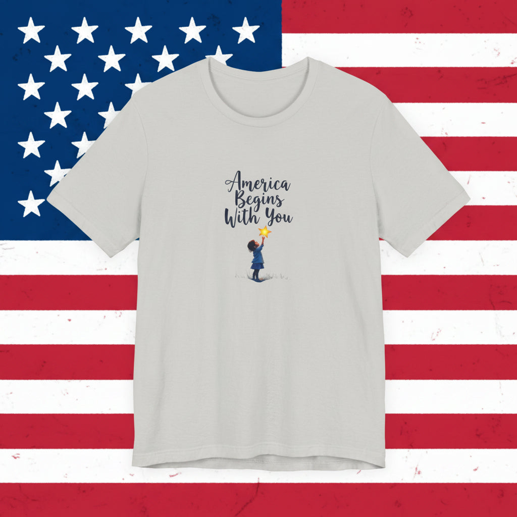 Gray t-shirt with 'America Begins With You' text and graphic on a patriotic  background