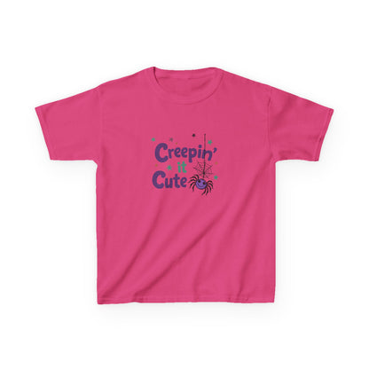 An orange short-sleeve kids' t-shirt with a 'Creepin' Cute' Halloween graphic on the chest, featuring purple text, a spider, and small stars, displayed on a clean white background. Heliconica/ hot pink