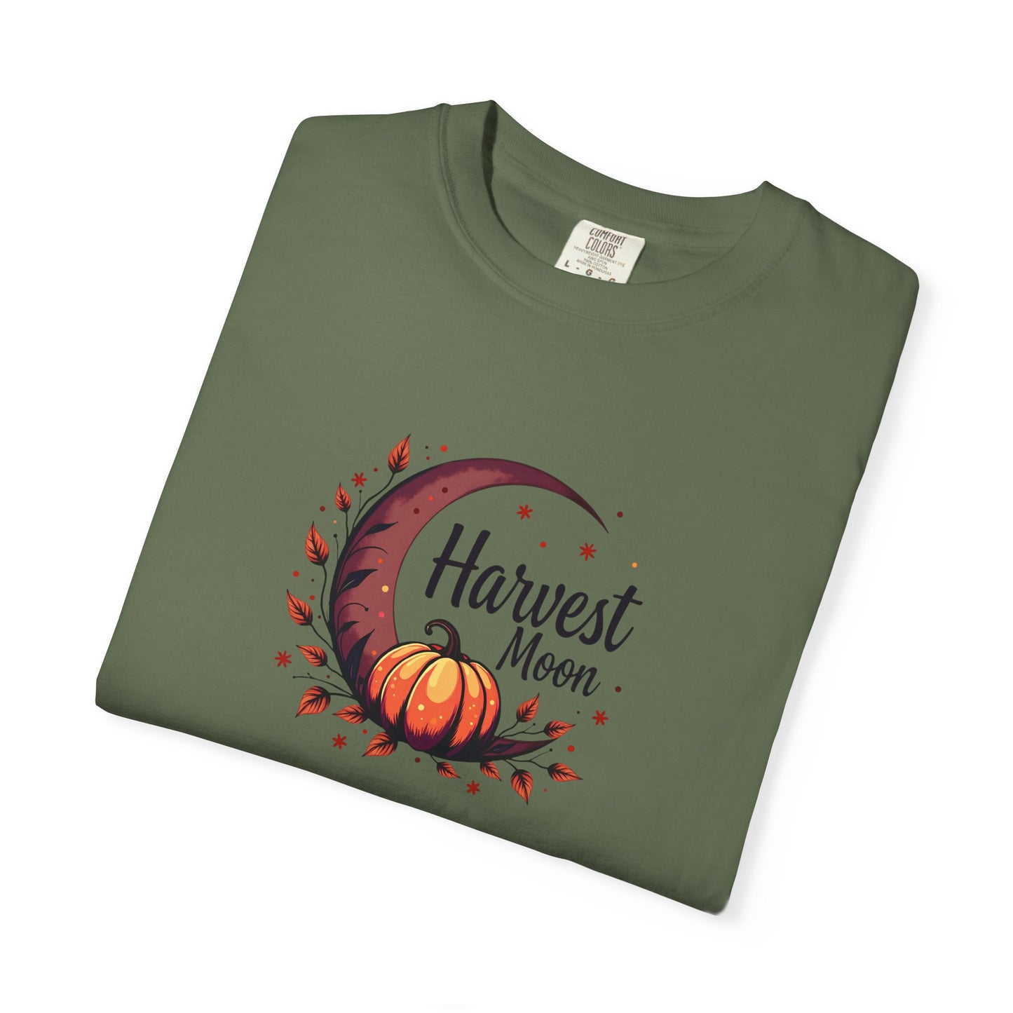 An olive green folded t-shirt with a 'Harvest Moon' graphic featuring an orange pumpkin, crescent moon, and autumn leaves on a white background.