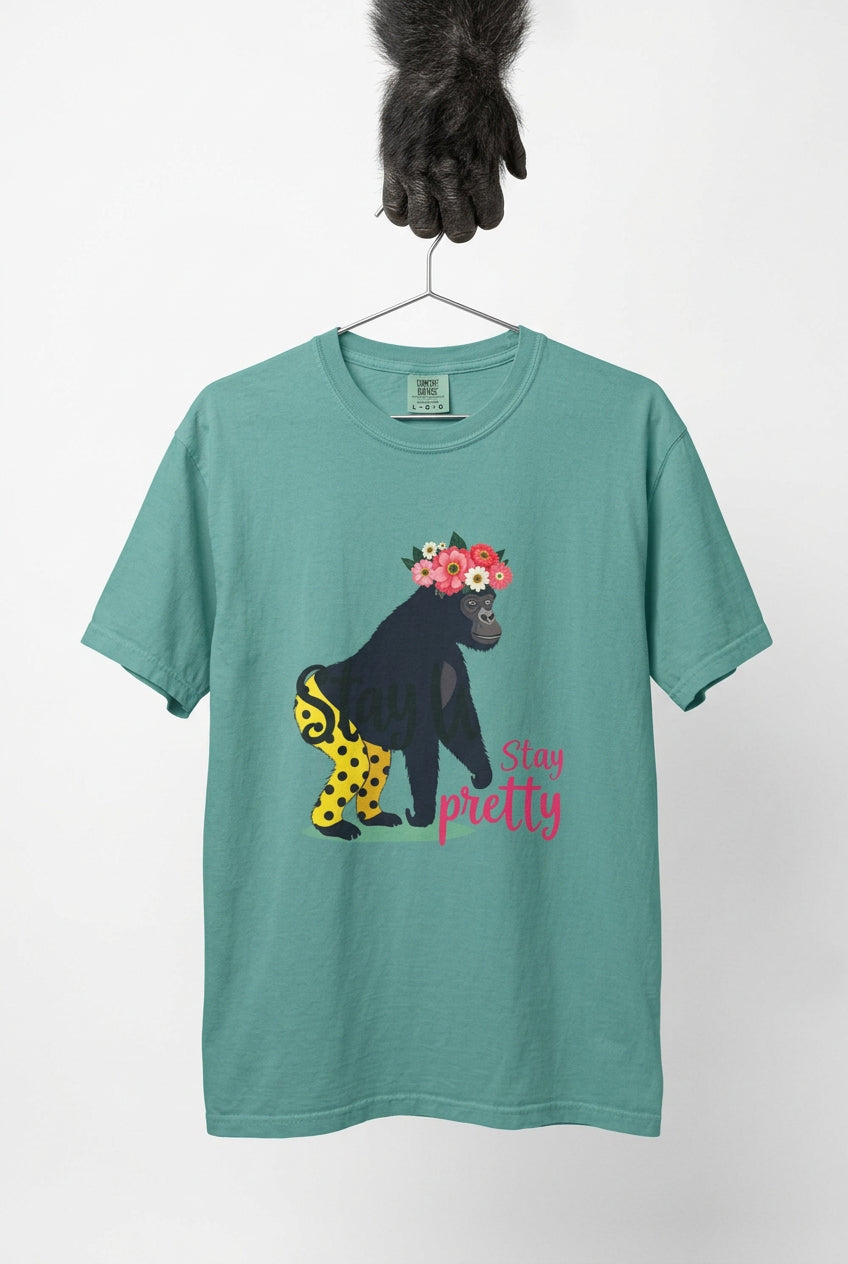 “Girl‑Girl™ gorilla wearing a flower crown and patterned shorts on a Seafoam unisex tee with the phrase ‘Stay Pretty.’” A gorilla hand holds the hanger.