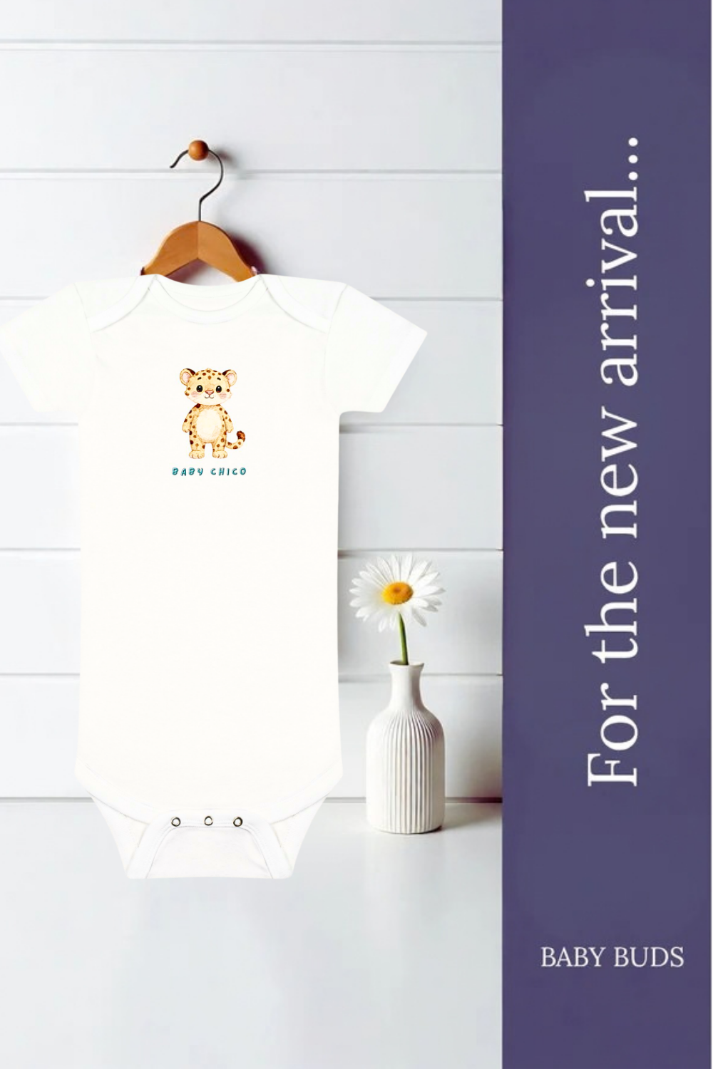 A white short-sleeved baby bodysuit hanging on a wooden hanger against a white paneled wall, with a small orange cheetah graphic and the text 'BABY Chico' on the chest. A small white vase with a daisy sits beside it. AI-generated