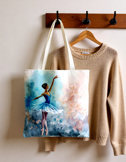 Tote bag with a ballerina design hanging on a wooden hook next to a beige sweater.